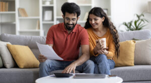 Indian couple together on a couch with paperwork and calculator, laptop and cell phone.